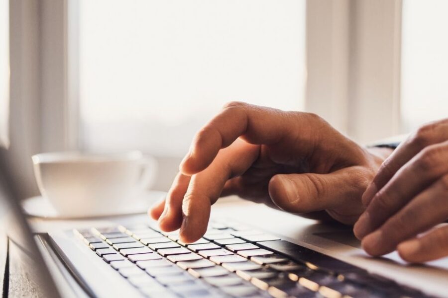 Je ziet de handen in beeld van een persoon die achter de laptop zit te werken.