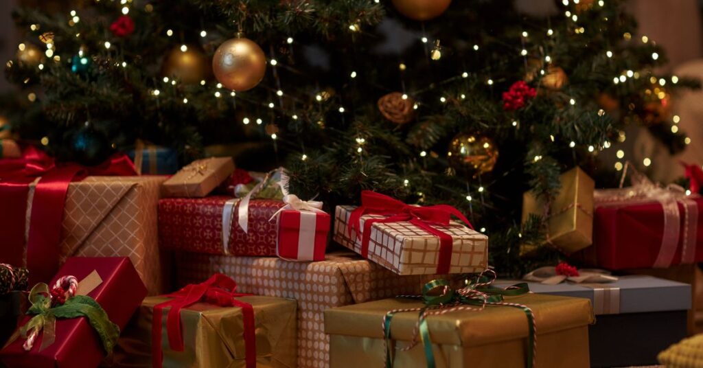 Onderkant van de kerstboom met verlichting. Daaronder liggen cadeaus in de kleuren rood goud wit.