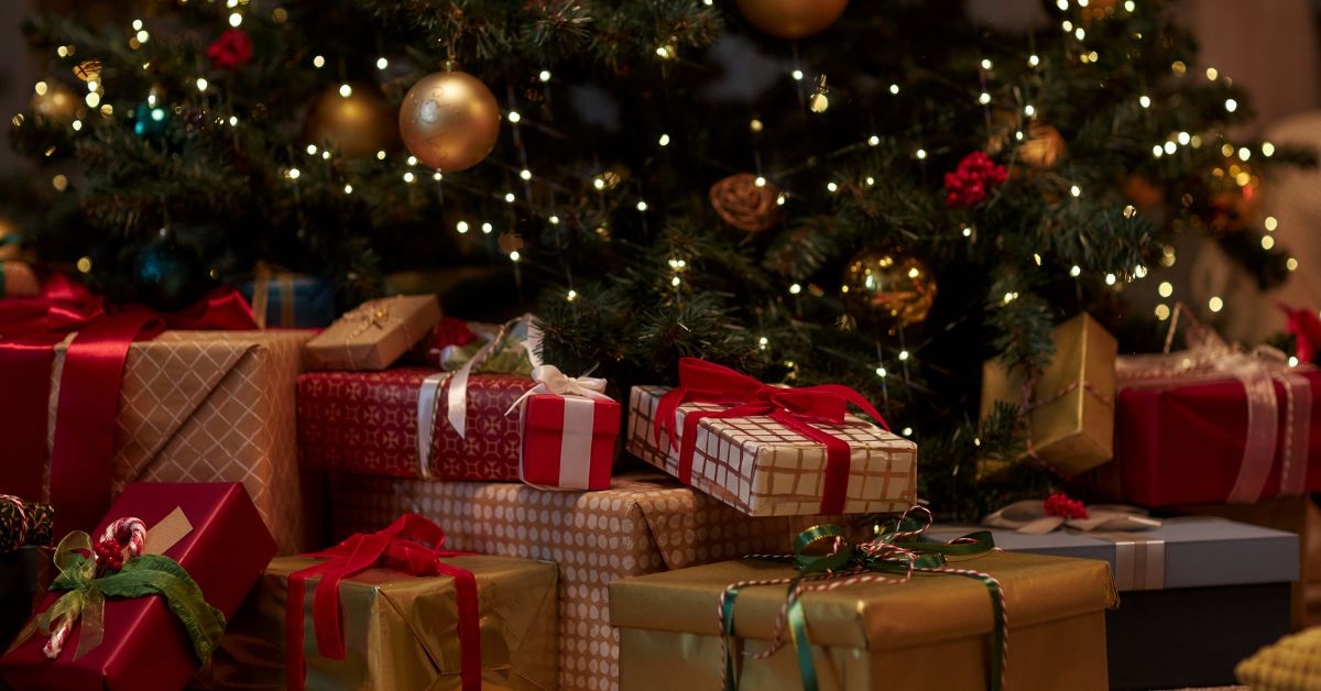 Onderkant van de kerstboom met verlichting. Daaronder liggen cadeaus in de kleuren rood goud wit.