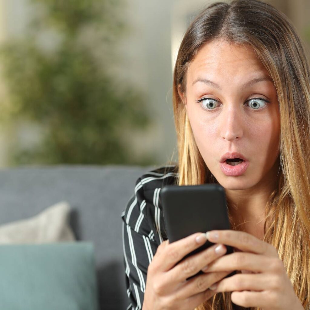 2 Vrouw kijkt verrast naar haar smartphone terwijl ze op de bank zit.